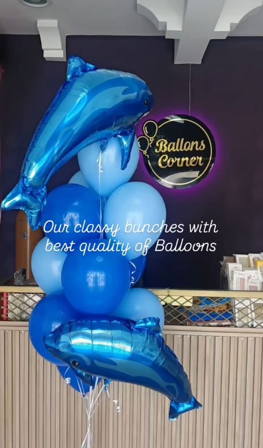 Blue dolphin foil balloon bunch in front of the Balloons Corner neon sign